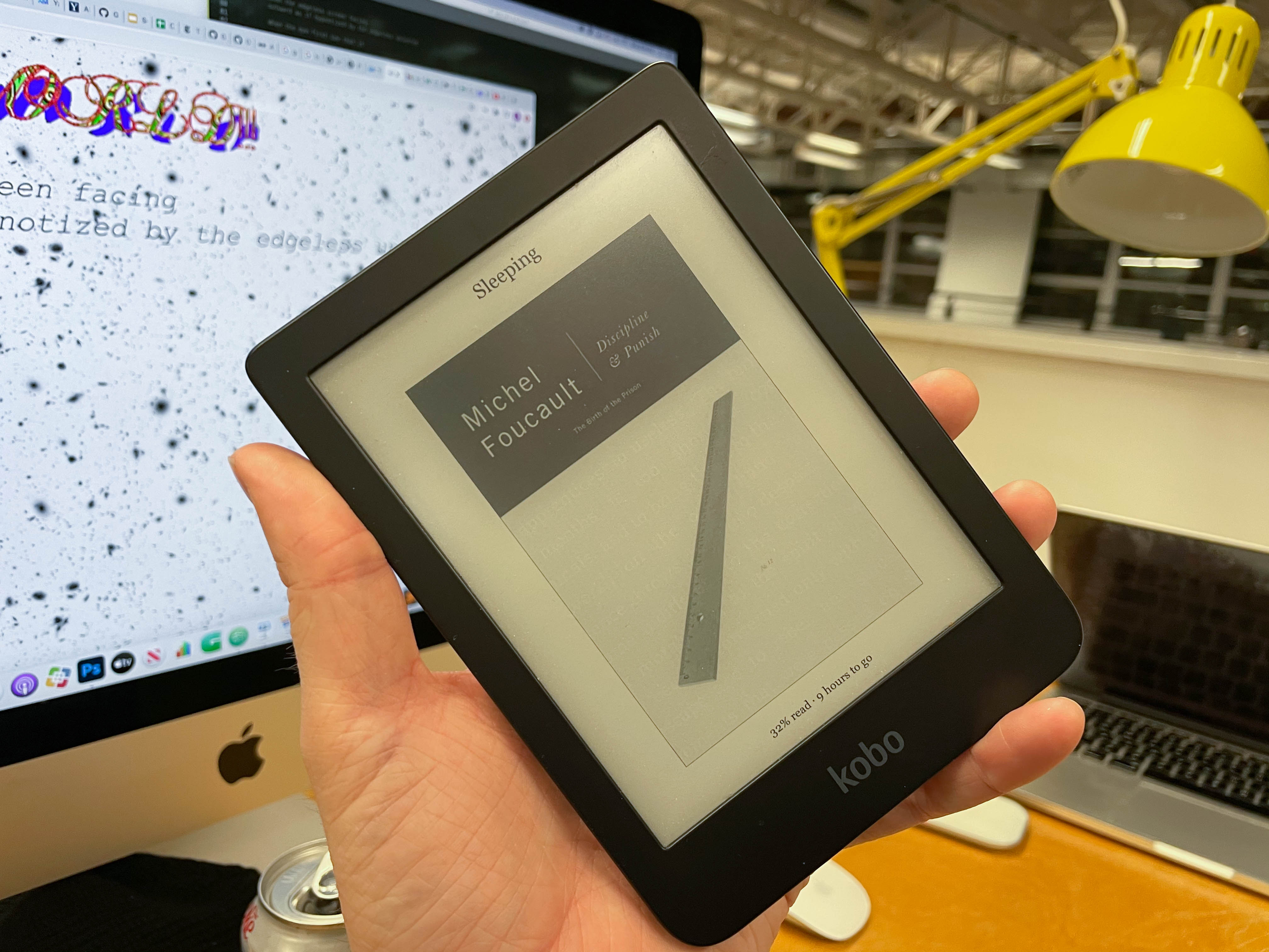 A kobo clara HD heald in from of a desk with a monitor display this very website.